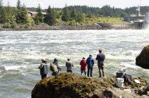 Six people standing on a rock facing Bradford Island fishing. 